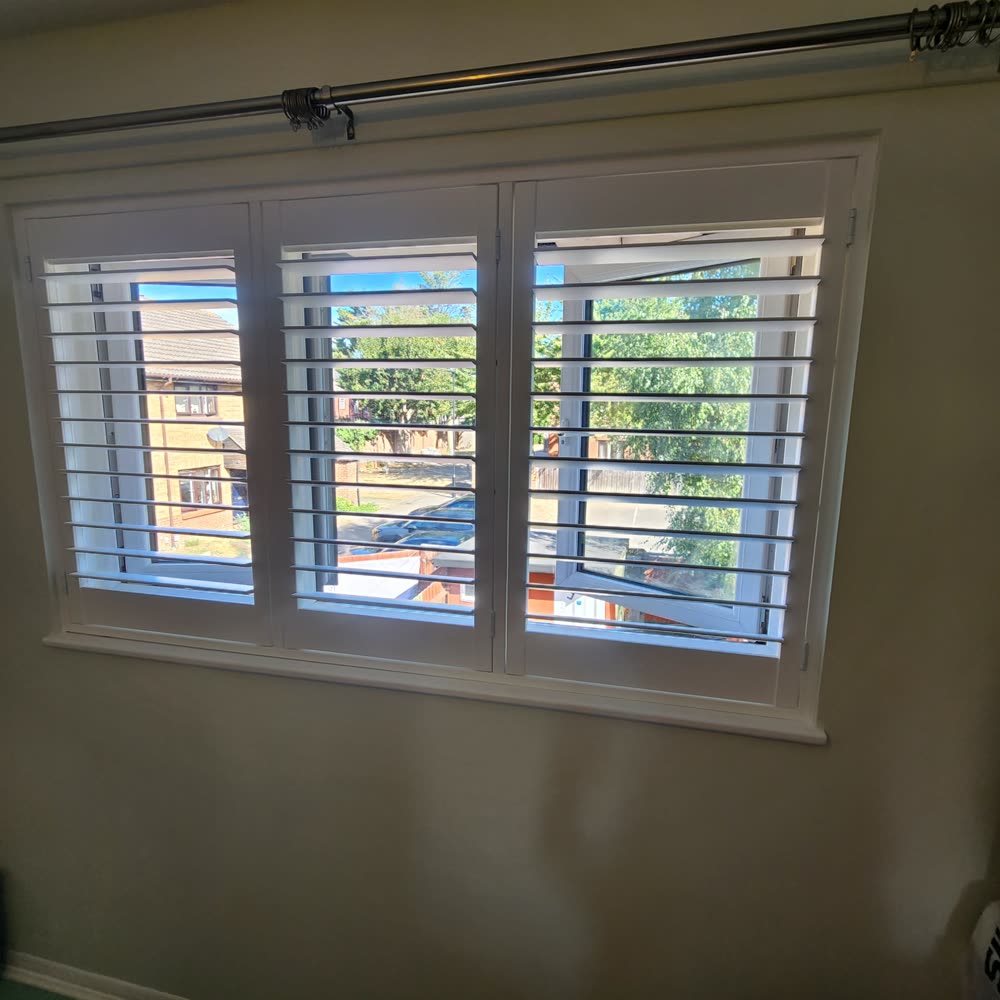 Three-panel white plantation shutters fitted to a bedroom window