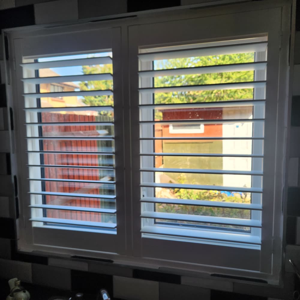 White full-height shutters fitted to a kitchen window, louvres angled for privacy